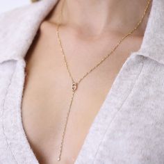 a woman wearing a gold necklace with a diamond on the bottom and a chain attached to it