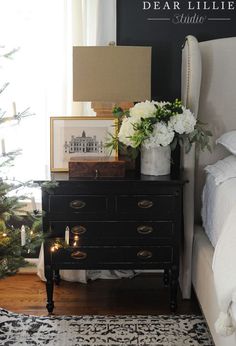 a bedroom decorated for christmas with white flowers and greenery on the dresser next to the bed