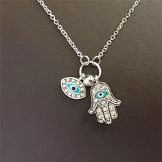 Introducing our Women's Fashion Jewelry Silver or Gold Plated Evil Eye Hamsa Hand Necklace, a stylish and symbolic accessory that combines the protective powers of the Evil Eye and the Hamsa Hand. The pendant of this necklace features a beautifully designed Hamsa Hand, a traditional symbol known for its protective qualities and ability to ward off negative energies. The Hamsa Hand is believed to bring luck, happiness, and blessings to the wearer. At the center of the Hamsa Hand pendant is the Evil Eye, a symbol used for centuries to protect against malevolent forces and to ward off negative influences. The Evil Eye is said to watch over the wearer, deflecting negative energy and bringing good fortune and protection. This necklace is available in either silver or gold plating, allowing you Spiritual Metal Necklaces With Charms, Spiritual Good Luck Charm Necklaces, Spiritual Charm Necklaces For Good Luck, Long Silver Spiritual Charm Necklaces, Silver Charm Necklaces With Adjustable Chain For Good Luck, Symbolic Pendant Necklace With Lobster Clasp, Silver Evil Eye Symbolic Necklace, Silver Symbolic Evil Eye Necklace, Silver Charm Necklace With Evil Eye For Good Luck