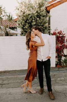 a man and woman standing next to each other in front of a white wall with red flowers