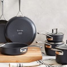 black pots and pans are sitting on a wooden cutting board next to each other