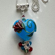 This is a small pendant created with an opal blue lampwork heart bead made by Jolene Wolfe in the UK.  There is a beautiful flower design on one side of the lampwork bead.  I accented it with 3 and 4 mm Swarovski caribbean opal, siam, and erinite bicone crystals, sterling bead caps, and tiny sterling spacer beads.  The sterling bail has a lovely little flower in the middle of it to continue the floral theme.  The pendant itself measures 2 inches from the top of the bail to the bottom of the dang Unique Blue Jewelry For Valentine's Day, Unique Blue Jewelry With Heart Charm, Handmade Whimsical Heart Pendant Jewelry, Handmade Heart-shaped Czech Glass Jewelry, Whimsical Czech Glass Necklaces For Gifts, Whimsical Czech Glass Necklaces As Gifts, Whimsical Czech Glass Necklace For Gift, Whimsical Heart-shaped Jewelry For Crafting, Beautiful Flower Designs