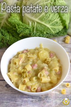 a white bowl filled with pasta next to lettuce on top of a wooden table