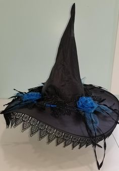 a black witches hat with blue flowers and lace on the bottom is sitting on a table