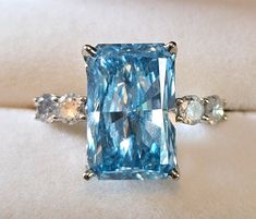 Gorgeous brilliant cut 8.59ct lab grown blue diamond ring bookended by .8ctw natural diamonds. Center lab grown diamond: Cut Cornered Rectangular Modified Brilliant 15.74x10.2x6.01mm SI1-SI2 Clarity Side natural diamonds: round brilliant cut 3.8 mm approximate .8ctw color H-J clarity I1-I2 Ring: 14ct white gold out of roundGorgeous brilliant cut 8.59ct lab grown blue diamond ring bookended by .8ctw natural diamonds. Center lab grown diamond: Cut Cornered Rectangular Modified Brilliant 15.74x10.2 Blue Radiant Cut Diamond Accented Jewelry, Blue Diamond Ring With Diamond Accents Emerald Cut, Luxury Blue Radiant Cut Diamond Ring, Blue Emerald Cut Diamond Ring With Diamond Accents, Blue Emerald Cut Diamond Ring With Accents, Gia Certified Blue Radiant Cut Jewelry, Blue Asscher Cut Diamond Ring With Accents, Dazzling Blue Diamond Cut Ring, Blue Radiant Cut Diamond Jewelry