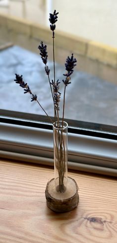 a vase filled with purple flowers sitting on top of a wooden table next to a window