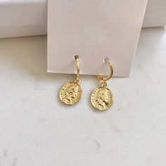 Dainty gold dangle coin earrings. These gold huggie earrings feature a tiny Italian lira coin charm. Delicate and yet eye catching. The ultimate accessory for every outfit, day to night. made of 14k gold plating over brass. Measurements: Diameter- 10mm Coin charm- 12xmm Shipping: Please allow 1-3 business days for your order to be processed and shipped. All orders are shipped in our customize box, gift ready. *Let me know if you have any questions and I will promptly respond Everyday Gold Plated Coin Jewelry, Gold Plated Charm Earrings, Nickel Free Gold Plated Round Huggie Earrings, Gold Plated Nickel-free Round Huggie Earrings, Gold-plated Charm Earrings, Yellow Gold Dangle Coin Pendant Jewelry, Yellow Gold Dangle Jewelry With Coin Pendant, Yellow Gold Coin Pendant Dangle Jewelry, Nickel Free Gold Plated Circle Earrings