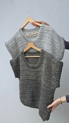 two knit sweaters hanging on clothes hangers, one in grey and the other in white