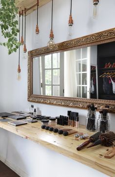 a wooden table topped with lots of makeup and other items next to a large mirror