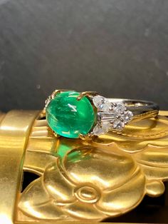 A ring that simply glows. Crafted in platinum and 18K yellow gold, the simply stunning piece is centered by an approximately 3.50ct natural cabochon Colombian emerald... and it truly does glow. Flanking the center stone an approximately 1cttw in G-I color and Vs1-2 clarity marquise, round and tapered baguette diamonds. This is a wonderful addition to anyone's collection of finer pieces. Ring is accompanied by a GIA laboratory report. -Best depiction of color is seen in the attached video. Dimens Luxury Oval Cabochon Emerald Ring, Luxury Domed Cabochons For Anniversary, Luxury White Gold Oval Cabochon Emerald Ring, White Gold Cabochon Emerald Ring Fine Jewelry, Luxury Yellow Gold Emerald Ring With Oval Cabochon, Fine Jewelry White Gold Emerald Cabochon Ring, Fine Jewelry White Gold Cabochon Emerald Ring, Oval Cabochon Platinum Rings, Elegant Oval Cabochons With Center Stone