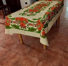 a table covered with a white and green floral design on top of a tile floor