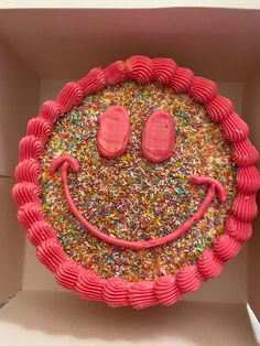 a pink cake with sprinkles and a smiley face on it in a box