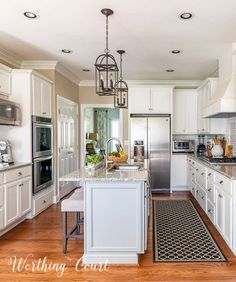 a large kitchen with white cabinets and stainless steel appliances, along with an island in the middle