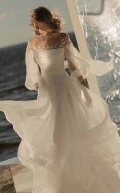 a woman in a white dress standing on the deck of a boat looking out at the ocean