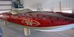 a man standing next to a red and white boat in a garage with two men looking at it