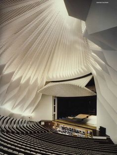 an auditorium filled with lots of seats next to a tall white building that has wavy walls