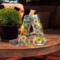 a glass letter sitting on top of a wooden table next to a potted plant