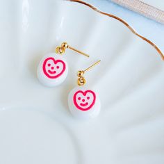 Bring a bright smile to your daily accessory game with these kawaii cute earrings. Featuring adorable handpainted smiley floral illustrations on round white polymer clay charm, these earrings radiate positivity and playfulness sure to put a smile on your face and those around you. Ideal for spring and summer events, casual outings, coffee dates or special occasions like Valentine's Day and Mother's Day, they appeal to women and girls of all ages who appreciate fun, feminine accessories. Lightweight and versatile, these earrings make thoughtful novelty gifts for friends, sisters, teachers, or nature lovers, and can effortlessly transition from everyday wear to more festive occasions. Their playful yet elegant design offers a delightful way to express personality and bring a pop of color to Trendy Pink Enamel Earrings, Playful Pink Earrings For Valentine's Day, Cute Heart-shaped Earrings For Everyday Wear, Cute Heart-shaped Everyday Earrings, Fun Nickel-free White Earrings, Cute Everyday Heart-shaped Earrings, White Kawaii Jewelry With Cute Design, White Heart Drop Earrings For Pierced Ears, Fun White Nickel-free Earrings