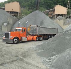 an orange semi truck parked in front of a pile of dirt and gravel at a quarry