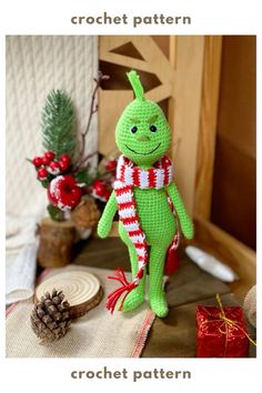 a crocheted green stuffed animal sitting on top of a table next to christmas decorations