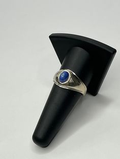 a silver ring with a blue stone in it on top of a black cone shaped stand