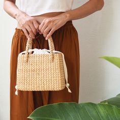 This handmade straw handbag is crafted from organic water grass hyacinth in Thailand by Thai women artisans. We designed a minimalist drawstring closure at the top to add a relaxed touch to this handbag. Ensure the safety of your belongings with our durable woven bag featuring a 100% natural dyed cotton inner lining, and a small pocket inside for your essentials, complemented by a ribbon closure adorned with unique pearl beads. It is more than just a handbag, it symbolises elegance and relaxation. Spring Rectangular Braided Bags, Spring Braided Rectangular Bag, Spring Braided Rectangular Bags, Summer Square Bag With Pearl Handle, Elegant Straw Beach Bag For Spring, Summer Square Bags With Pearl Handle, Elegant Spring Beach Bag In Natural Color, Rectangular White Straw Bag, Elegant Natural Beach Bag For Spring