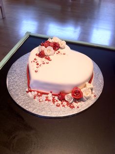 a white heart shaped cake with red and white flowers on the top is sitting on a silver platter