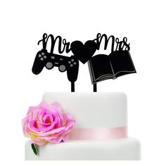 a white cake with a pink rose and two black hearts on top that say mr and mrs