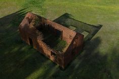 an old building with grass growing out of it's sides in the middle of a field