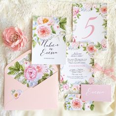 the wedding stationery is laid out on a bed with flowers and pink envelopes