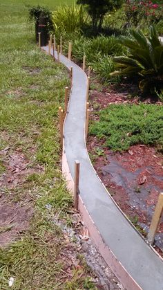 a concrete walkway in the middle of some grass and bushes with wooden posts on each side