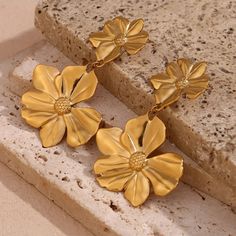 Transform any outfit with these Gold Flower Drop Earrings! These unique earrings feature delicate flowers that add a touch of femininity, and the dangle design creates movement and elegance. Elevate your style and make a statement with these gorgeous earrings. DETAILS & SIZE Sold as a pair Finish: 18K gold plate Material: Stainless Steel Measurements: 2.5"x1.5" Weight: 19.3 grams Comes with friction earring backs Waterproof, tarnish-resistant, and nickel free Shop Earrings to curate your ear stack! Flower Earrings Dangle, Gold Flower Earrings, Enchanted Jewelry, Stud Fashion, Flower Drop Earrings, Earring Stand, Long Drop Earrings, Flower Plates, Gold Flower