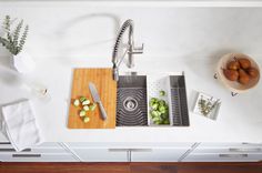 a kitchen sink with cutting board, knife and other items on the counter next to it