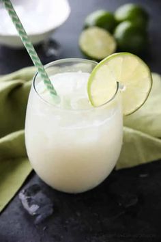 a close up of a drink in a glass with a straw and limes on the side