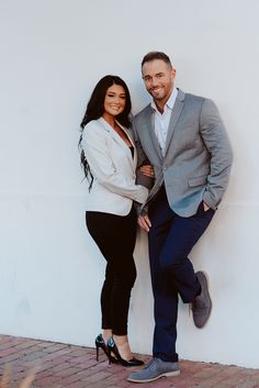 a man and woman standing next to each other near a white wall smiling at the camera