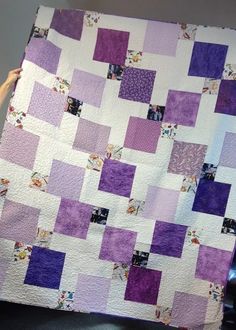 a person holding up a purple and white quilt