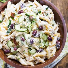 a wooden bowl filled with pasta salad and cucumbers