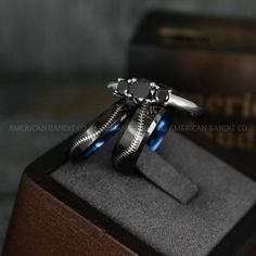 two wedding rings are sitting on top of each other in a wooden box with black and blue accents