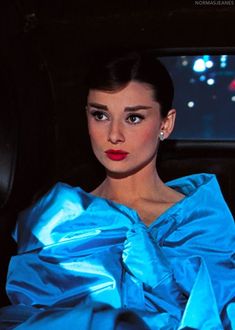 a woman sitting in a car wearing a blue dress and red lipstick on her lips