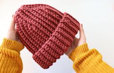 two hands holding up a knitted beanie in front of a white background,