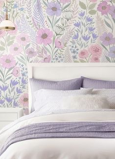 a white bed with purple and pink flowers on the wall next to it's headboard