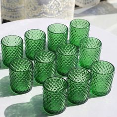 many green glasses are sitting on a white table with lace doily in the background