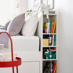 a white bed sitting next to a book shelf with books on it's sides