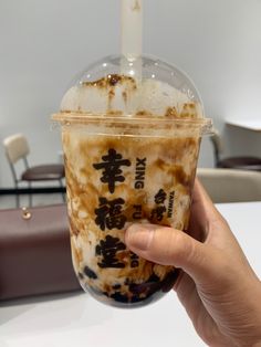 a person holding up a drink in a plastic cup with writing on the side and a candle sticking out of it