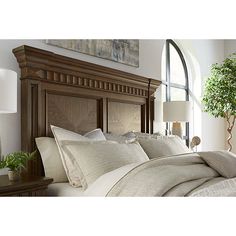 a bed with white sheets and pillows in front of a wooden headboard next to a window