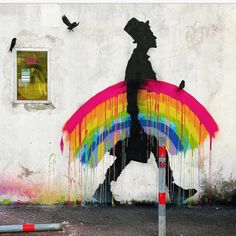 a man with a rainbow umbrella is painted on the side of a building, and birds are flying around