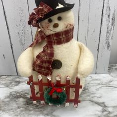 a snowman with a hat and scarf on standing in front of a white fence