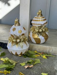 two white and gold christmas ornaments sitting on the front steps with leaves scattered around them