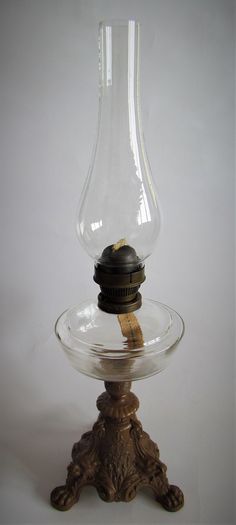 an old fashioned oil lamp sitting on top of a glass stand with a wooden base