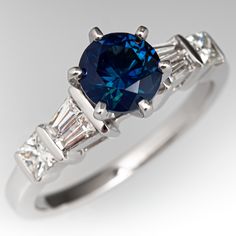 This beautiful ring is centered with one (1) round brilliant cut natural sapphire weighing 1.30 carats that is set into a six-prong head. The shoulders of the ring are each accented with two (2), channel set, tapered baguette cut diamonds and one (1), channel set, princess cut diamond. The ring measures 7.9mm at the top, rises 8.5mm above the finger, tapering to 1.8mm wide and 1.2mm thick at the base of the shank. This ring is currently a size 6.75. Classic Sapphire Diamond Ring Gia Certified, Gia Certified Sapphire Diamond Ring In Timeless Style, Gia Certified Timeless Sapphire Diamond Ring, Classic Formal Diamond Ring With Lab-created Sapphire, Exquisite Sapphire Diamond Ring With Vvs Clarity, Classic Sapphire Diamond Ring With Brilliant Cut, Luxury Sapphire Ring With Lab-created Center Stone, Luxury Lab-created Sapphire Ring With Prong Setting, Luxury Rings With Brilliant Cut Lab-created Sapphire